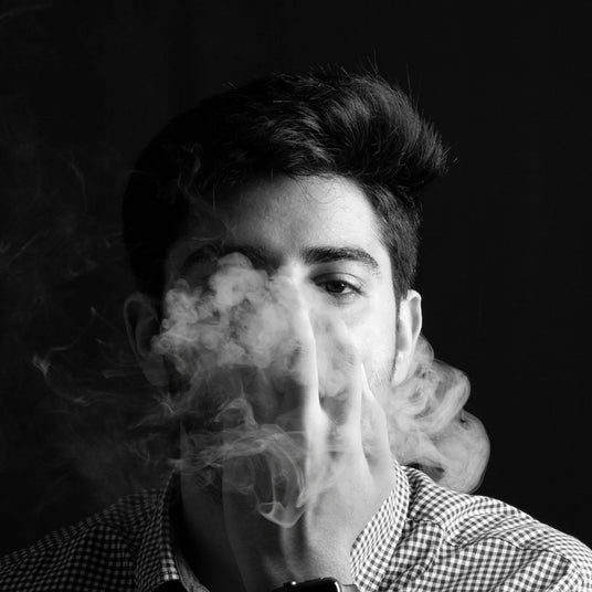 Man vaping with his hand in front of his face, in black and white.