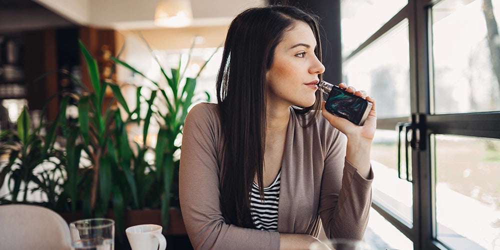Woman vaping looking out of a window.